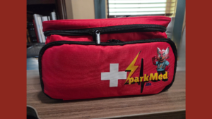 Red four-compartment SparkMed.life motorcycle first aid kit with white cross and lightning bolt graphic on front panel.